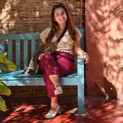 Mulher sentada no banco azul com roupas coloridas e bolsa tiracolo