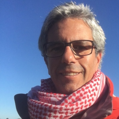 Pessoa com lenço keffiyeh vermelho e branco e óculos com céu azul ao fundo