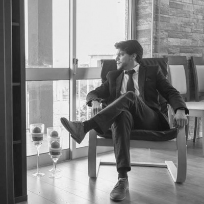 Homem em fato sentado numa cadeira de braços de madeira com almofada