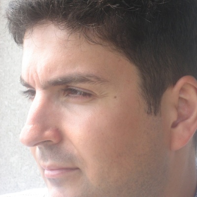 Homem de perfil com cabelo castanho escuro e pele clara, fundo neutro