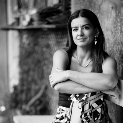 Mulher com vestido geométrico e brincos encostada em parede rústica