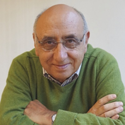 Homem de idade com suéter verde e óculos, sorrindo para a câmera