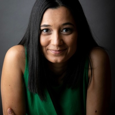 Mulher com camiseta verde sem mangas e cabelo preto liso num fundo cinzento