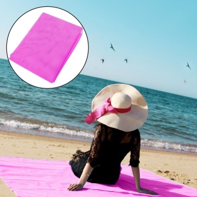 Pessoa sentada numa toalha rosa na praia com chapéu branco e mar ao fundo