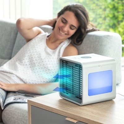 Ar condicionado portátil branco com luz azul em mesa de madeira junto a sofá cinzento e mulher sorridente