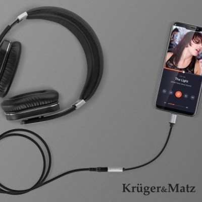 Auscultadores pretos conectados a smartphone a tocar música, fundo cinzento e marca Krüger&Matz