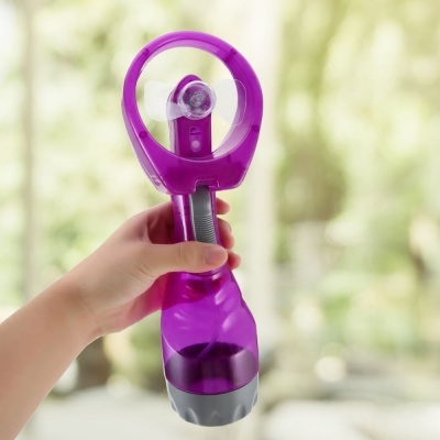 Ventilador portátil roxo com base cinza segurado por mão, fundo desfocado de natureza