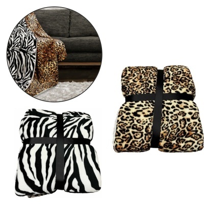 Dois cobertores macios com padrões de pele de animal, cobertor de onça e cobertor de zebra, enrolados e amarrados com fita preta, detalhe do cobertor de onça num sofá cinza.