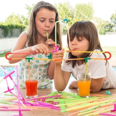 Duas crianças a brincar com canudos coloridos e beber sumos em copos transparentes perto da piscina.