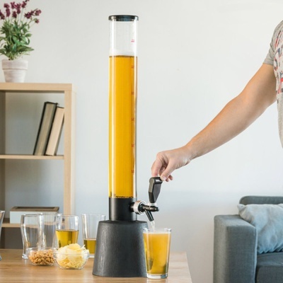 Dispenser de bebida amarelo com torneira numa mesa com copos e petiscos