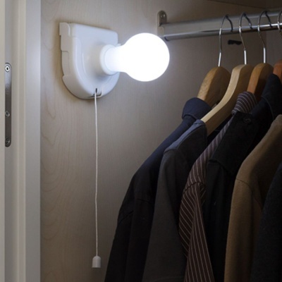 Abajur de parede branco com lâmpada acesa num armário com casacos e camisas
