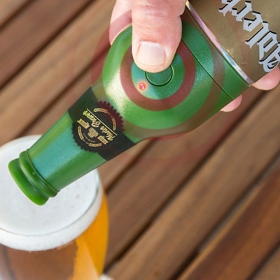 Garrafa verde de cerveja sendo despejada em caneca com cerveja clara, rótulo preto e dourado, fundo de madeira