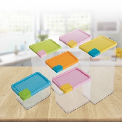 Caixas de plástico transparentes com tampas coloridas e fechos, sobre mesa de madeira clara na cozinha