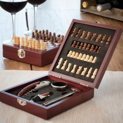 Conjunto de xadrez em madeira com peças e acessórios para vinho em caixa de madeira aberta, taças de vinho e garrafas ao fundo