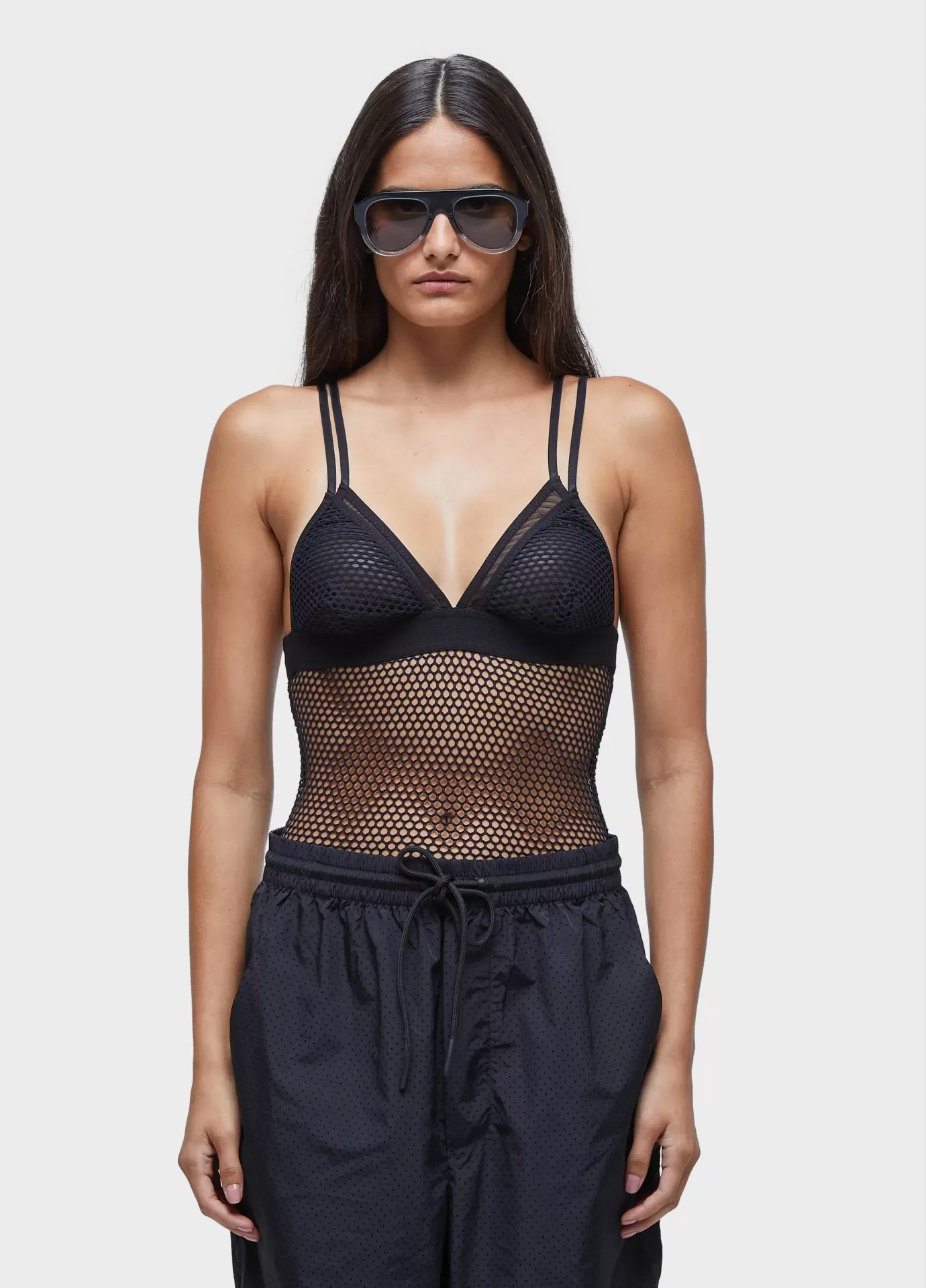 Body under mix tela e tule Mulher de cabelo comprido usa óculos escuros, body preto de malha e calças pretas com cordão
