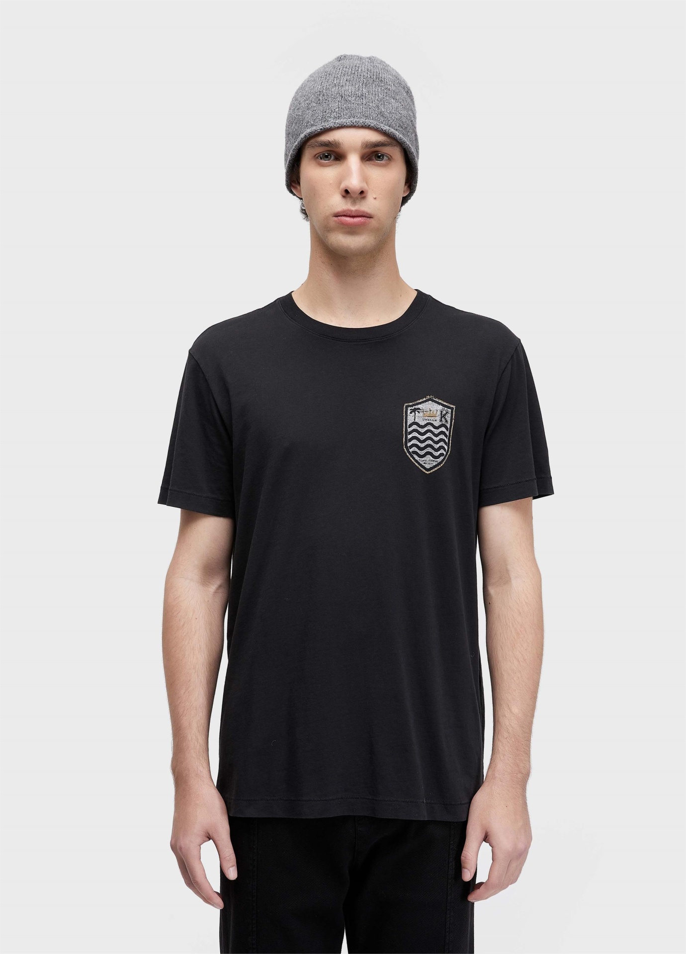T-shirt Soft Used Brasao Destroyed Osklen Pessoa com t-shirt preta com emblema prateado, gorro cinza e calças pretas