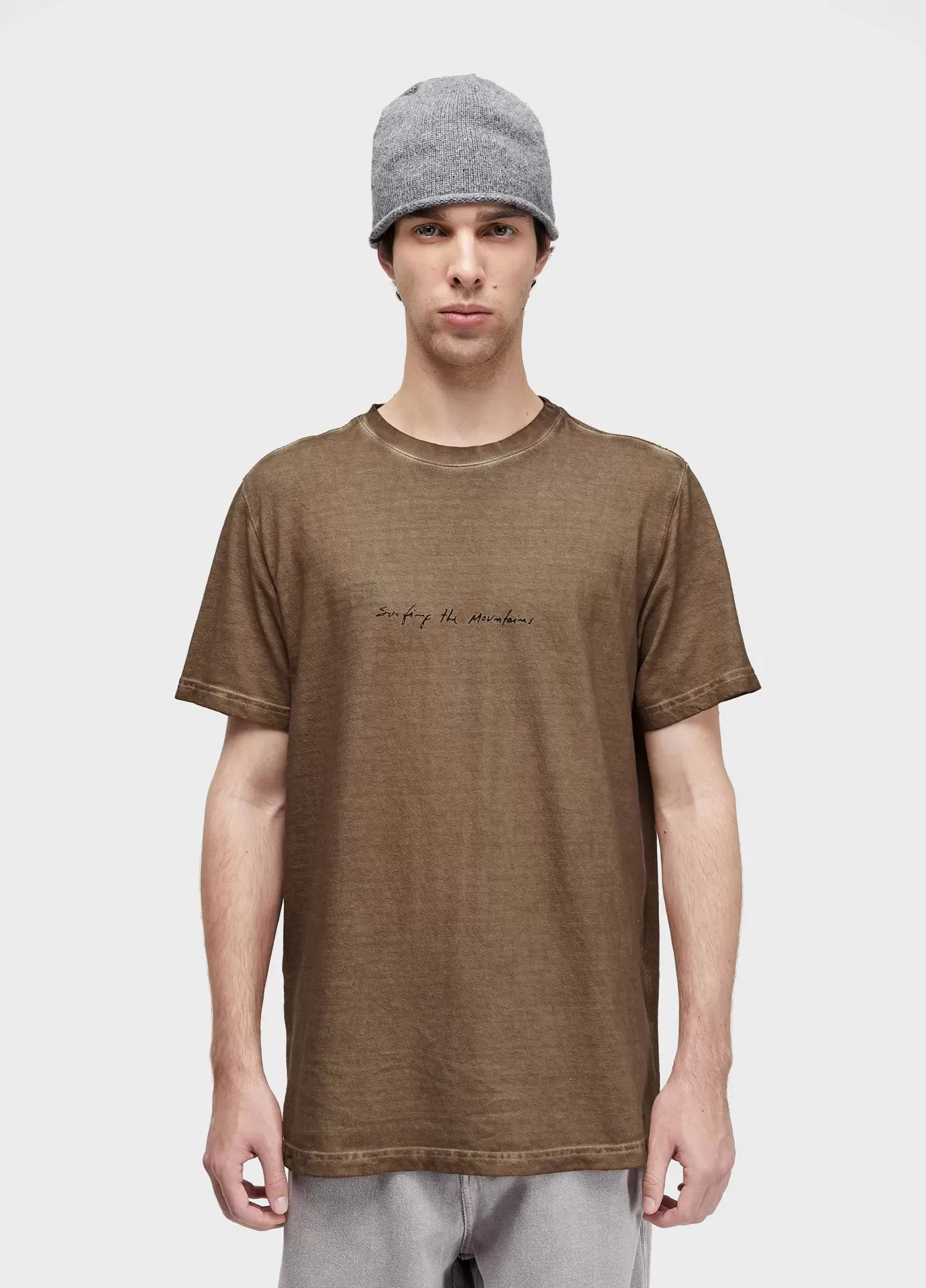Homem com camisola castanha e gorro cinzento frente a fundo branco.