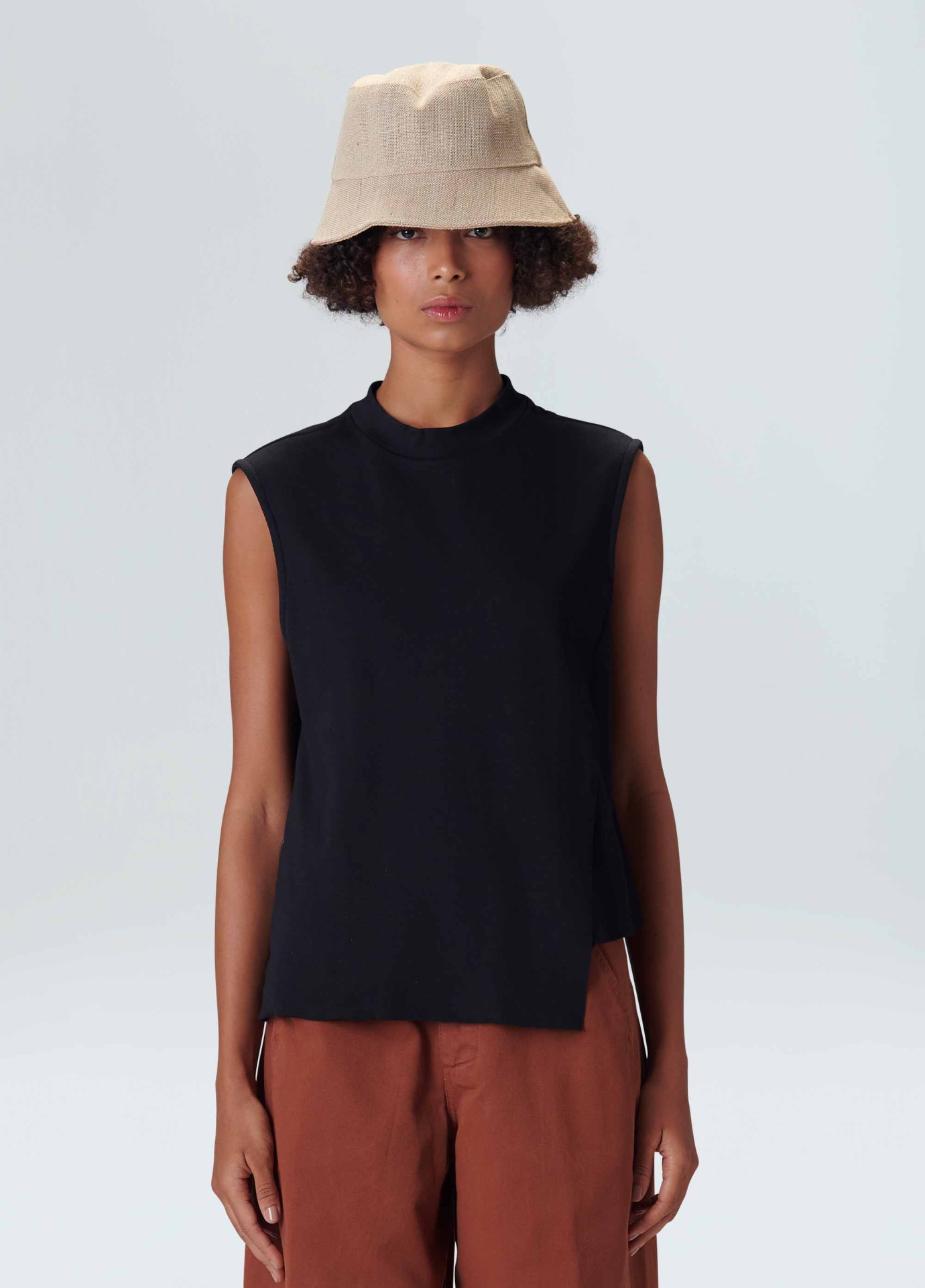 Sleeveless Diagonal Black Osklen Modelo com regata preta sem mangas, calças castanhas e chapéu bucket bege