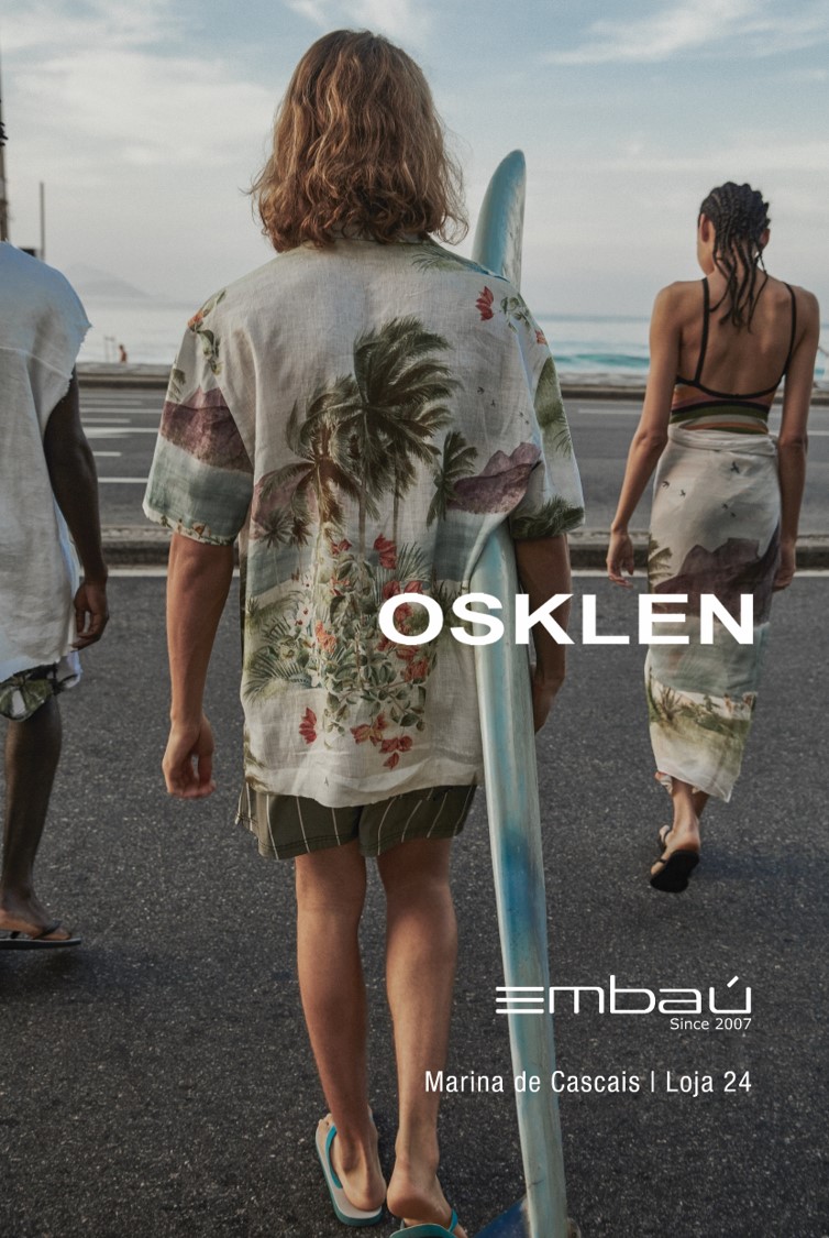 Nova colecção Primavera-Verão Osklen na Embaú Três pessoas de costas na praia, uma com camisa tropical e prancha de surf, textos OSKLEN e embau visíveis.
