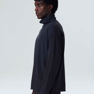 Homem com suéter de gola alta preto em fundo cinza claro