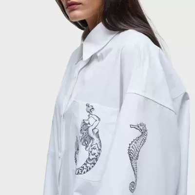 Camisa branca oversized com estampas de sereia e cavalo-marinho e óculos de sol âmbar