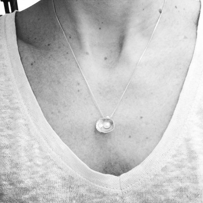 Colar prateado com pérola no pescoço com camisa branca