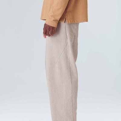 Vista lateral de calças bege claro largas com camisa castanha e sapatos bege