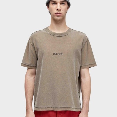 Homem com camisola bege OSKLEN, calças vermelhas e gorro cinza em fundo branco
