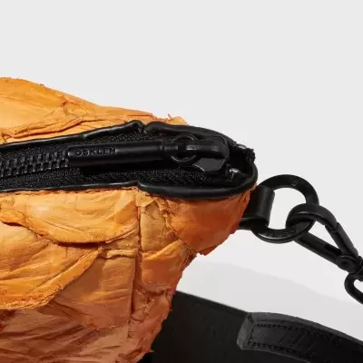 Detalhe de mala laranja com fecho preto e alça preta ajustável