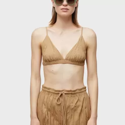 Mulher com top bege e calças largas, óculos de sol verde claro.