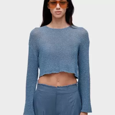 Mulher com camisola de malha azul e calças largas azuis com acabamento desfiado e óculos de sol castanhos.