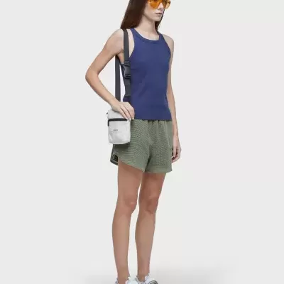 Mulher com camisola azul, calções verdes, sandálias brancas e bolsa branca ao ombro