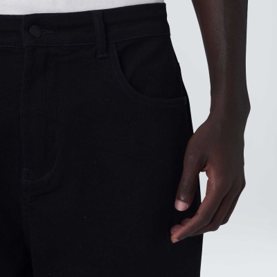 Calças pretas e parte da mão de uma pessoa com t-shirt branca sobre fundo cinzento.