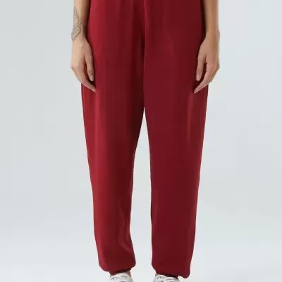 Calças vermelhas com cós elástico largo usadas com sapatilhas brancas sobre fundo cinzento