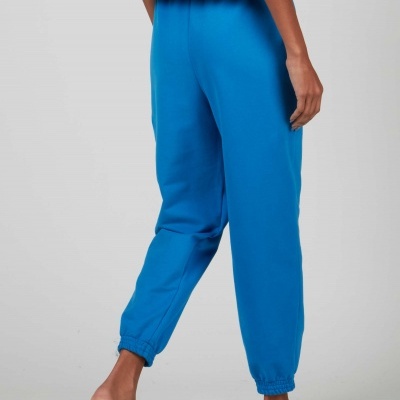 Calças de treino azuis com bainhas elásticas nos tornozelos, usadas por uma pessoa com chinelos brancos.