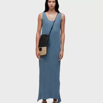 Mulher com vestido longo azul, sandálias bege, bolsa transversal preta e bege, colar prateado com pendente em forma de folha