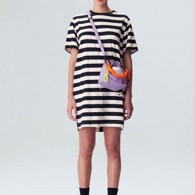 Mulher vestindo vestido de riscas pretas e brancas com bolsa lilás e detalhes coloridos, em fundo branco.