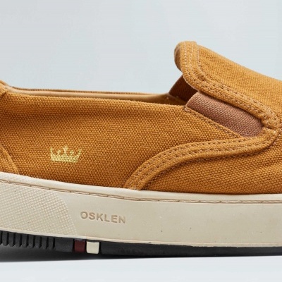 Ténis slip-on de lona castanha com sola branca e marcas OSKLEN e coroa dourada