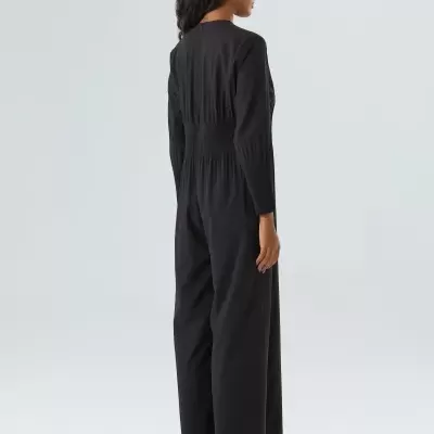 Mulher de costas a usar macacão preto de manga comprida e sandálias brancas