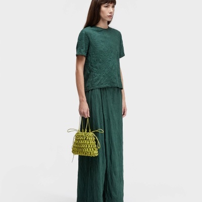 Mulher veste conjunto verde, segura mala amarela e calça sandálias.