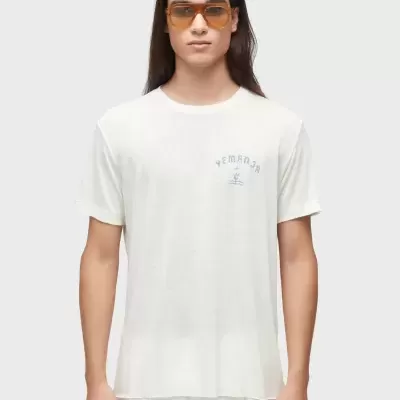 T-shirt branca com estampa azul claro YEMANJÁ usada por modelo com óculos laranja.