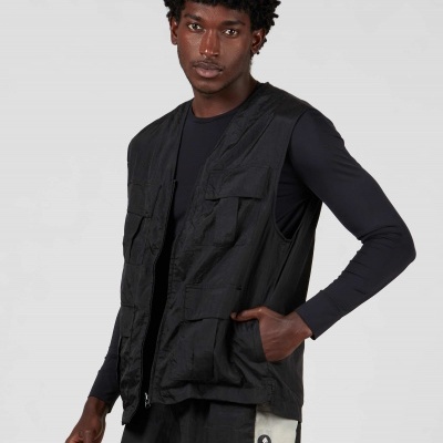 Homem veste colete preto com bolsos e calças pretas com faixa branca