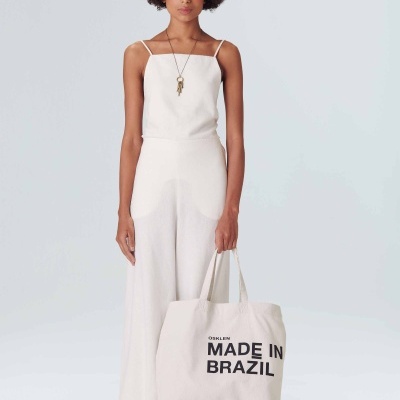 Mulher vestindo roupa branca e segurando mala de tecido com texto preto