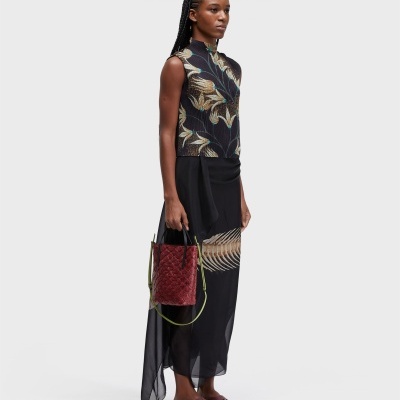 Mulher de vestido preto transparente e top floral, com sandálias castanhas e mala vermelha.