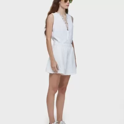 Mulher de pé com macacão branco, ténis brancos e óculos de sol amarelos