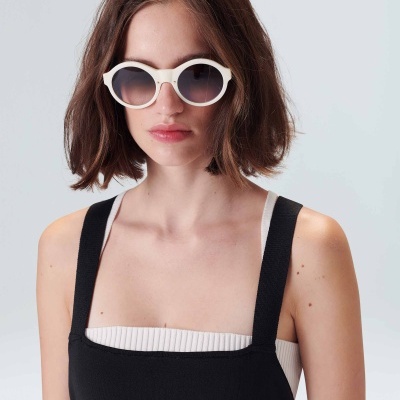 Mulher com vestido preto e top branco, usando óculos de sol redondos brancos