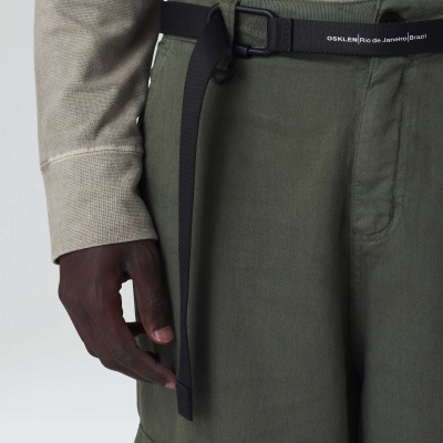 Parte inferior de pessoa com calças verdes, cinto preto com texto e camisa bege clara