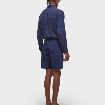 Homem vestido com camisa e calções azuis de costas em fundo branco.