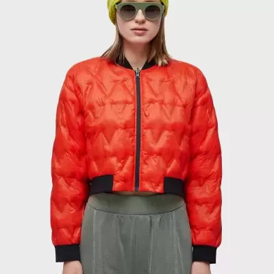 Casaco vermelho acolchoado com calças cinza, gorro verde e óculos de sol.