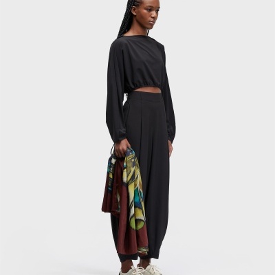 Mulher de blusa cropped preta e calças largas pretas com capulana colorida nas mãos